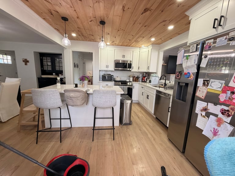 Modern kitchen with white cabinetry, wooden ceiling, stainless steel appliances, and bar seating with upholstered chairs
