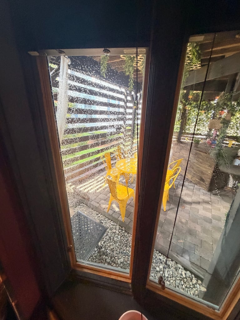 View through glass doors to outdoor patio with yellow chairs, white horizontal slat fence, and green plants