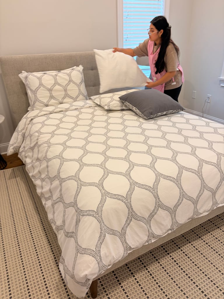 Woman arranging pillows and bedding with geometric pattern on a bed in a bright bedroom