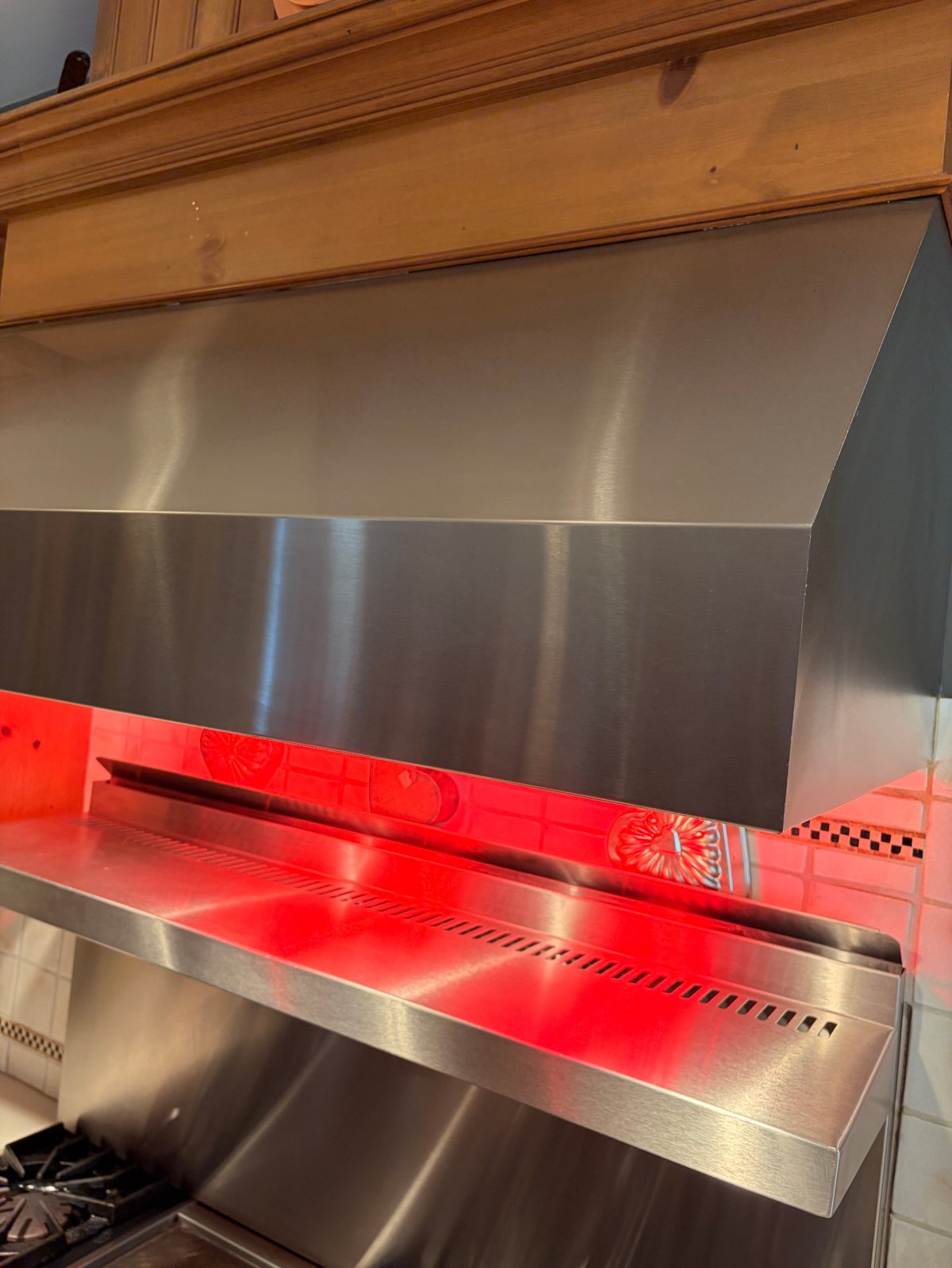 Stainless steel range hood with red LED trim and wooden cabinet frame mounted on kitchen wall