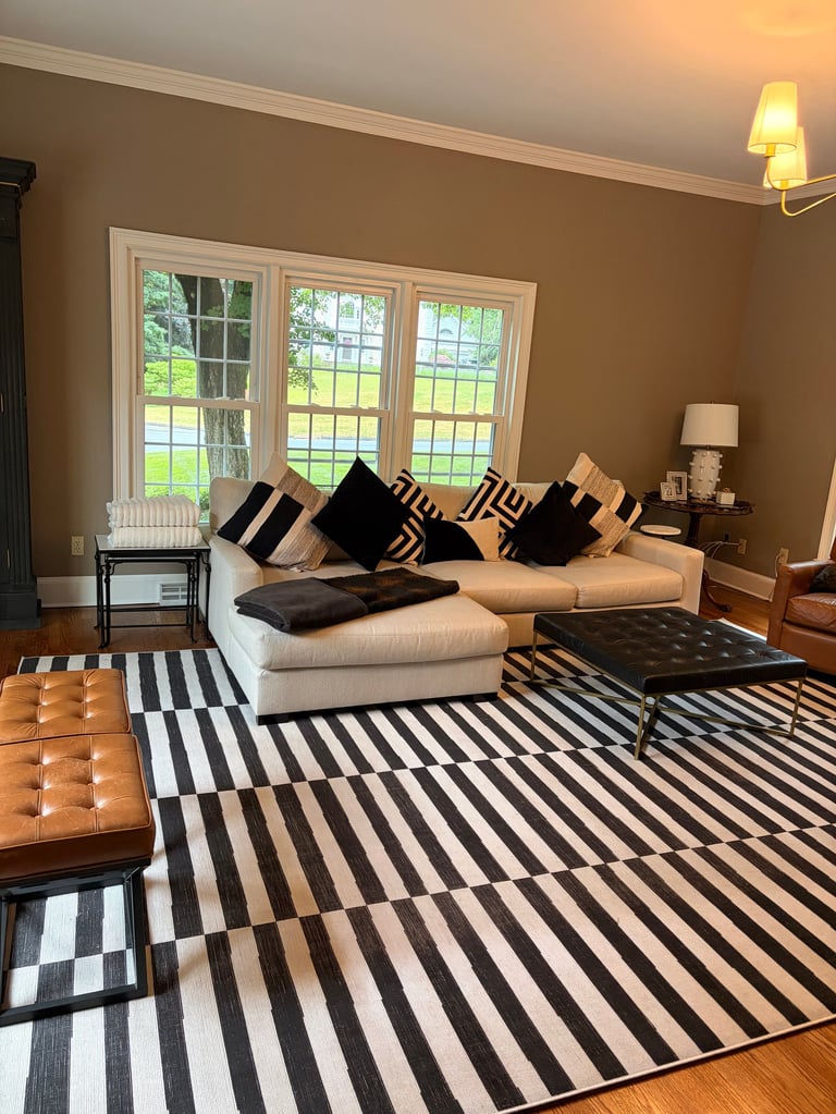 Modern living room with beige sectional sofa, black and white striped rug, geometric pillows, and french doors overlooking a garden
