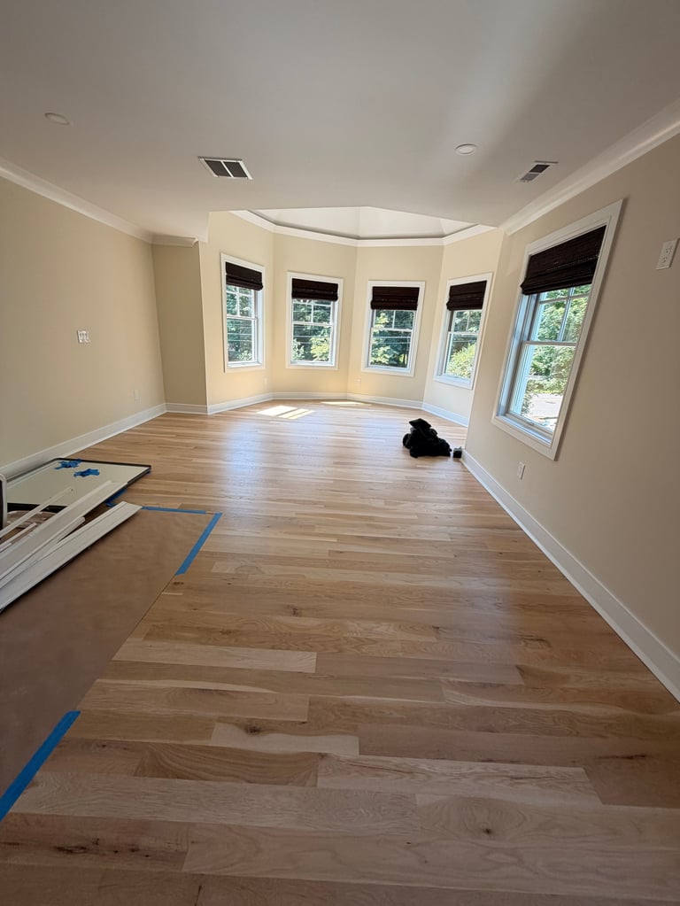 Empty room with curved bay windows, hardwood flooring, cream walls, and recessed ceiling lights during renovation.