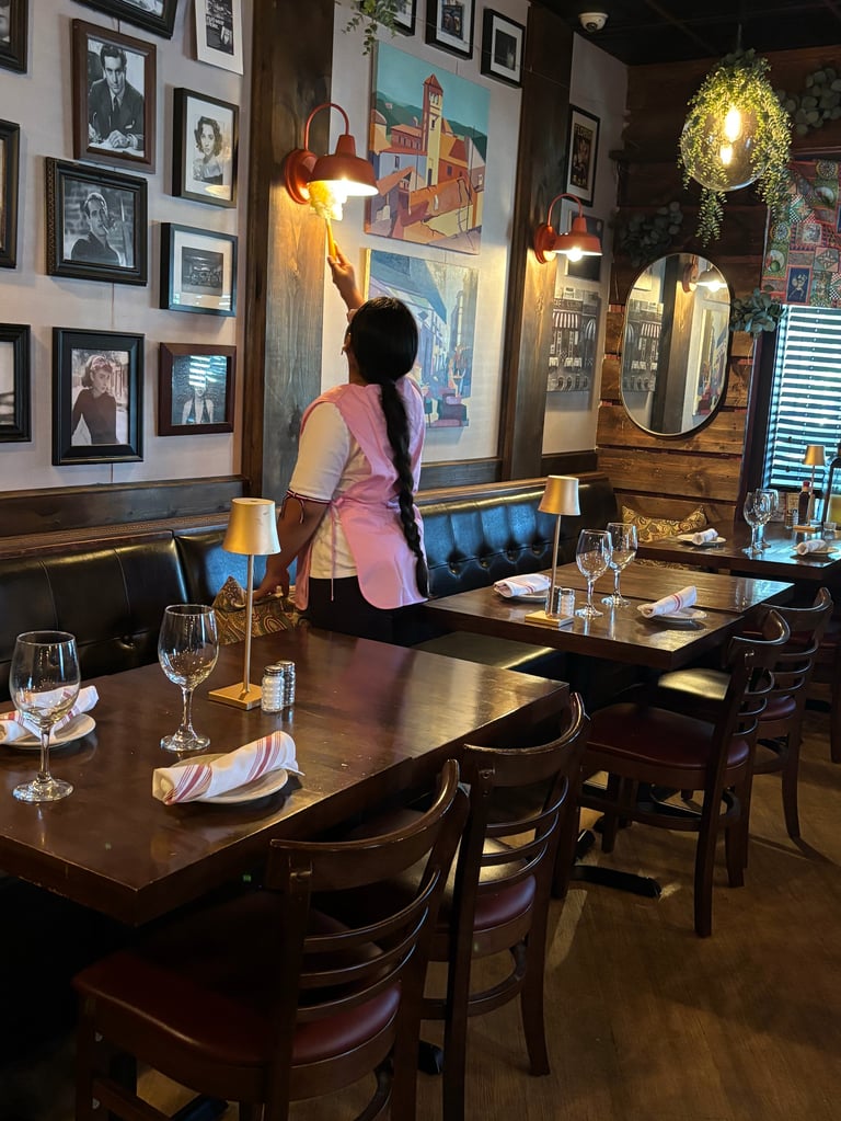 Woman in pink top standing at dining table in restaurant with framed artwork on walls and warm lighting