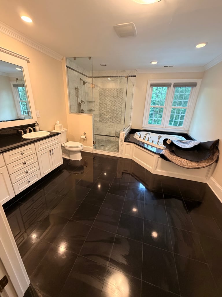 Luxury bathroom with white cabinetry, black tile flooring, glass shower enclosure, soaking tub, and large windows