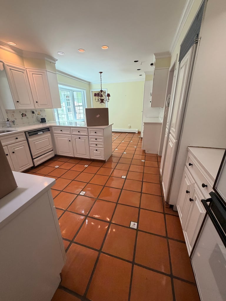 Spacious kitchen with white cabinetry, terracotta tile flooring, and yellow accent walls leading to a dining area.
