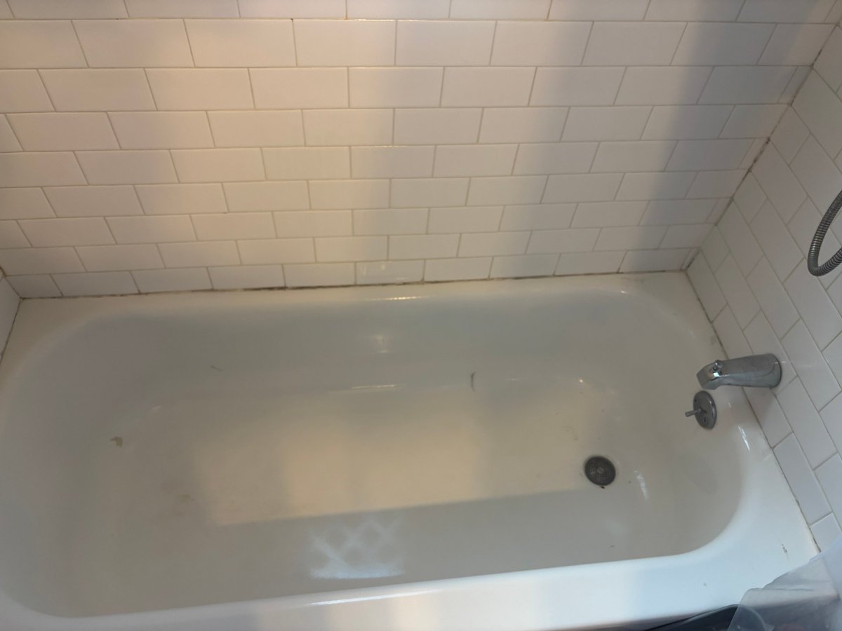 Empty white bathtub with tiled walls and chrome faucet, viewed from above