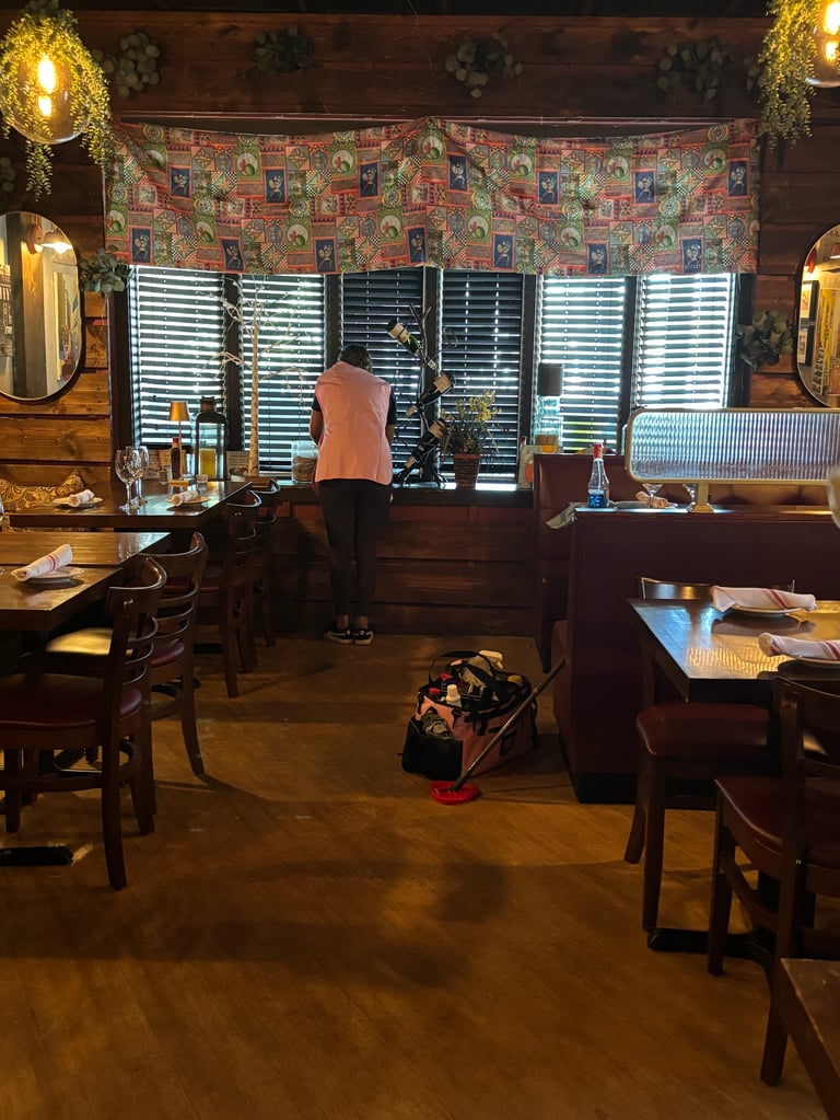 Person in coral shirt working at vanity desk in warm-lit room with wooden furniture, decorative wall tapestry, and shuttered windows