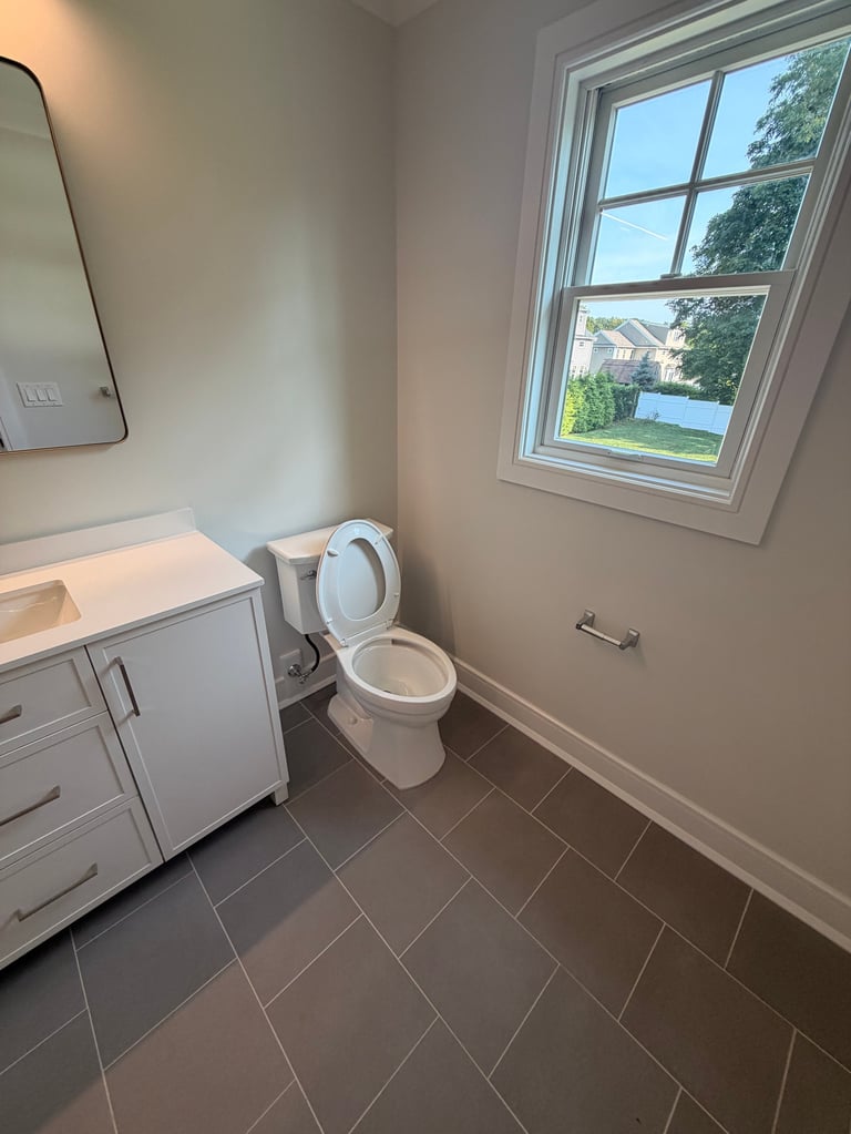 Modern bathroom with white vanity, toilet, and window overlooking suburban landscape