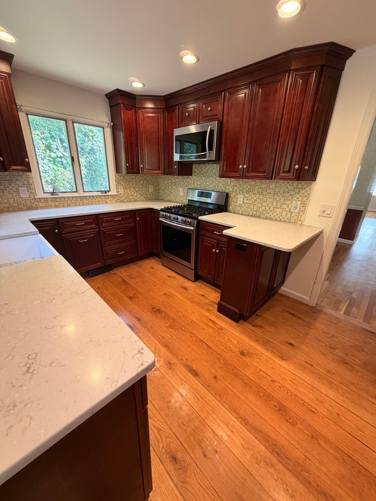 Modern kitchen with dark red cabinets, white marble countertops, stainless steel appliances, beige backsplash, and wood flooring
