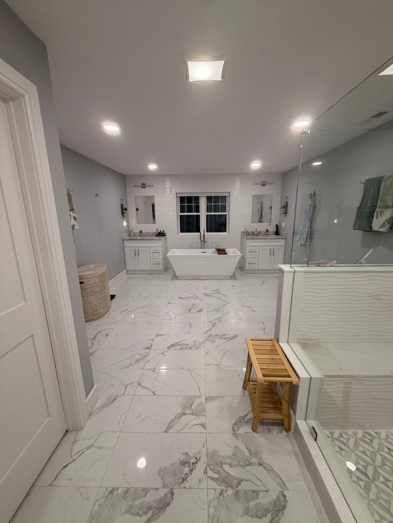 Modern luxury bathroom with marble flooring, dual vanities, freestanding tub, and walk-in shower with glass enclosure