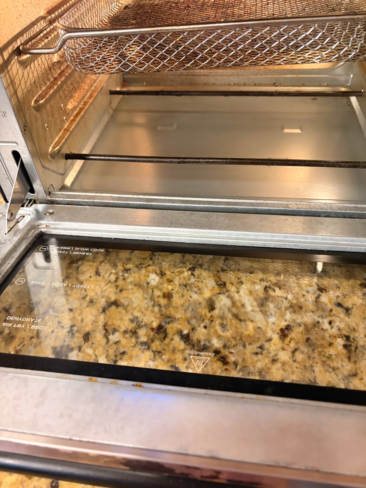 Open toaster oven with removable wire rack and baking tray, showing interior and granite countertop below