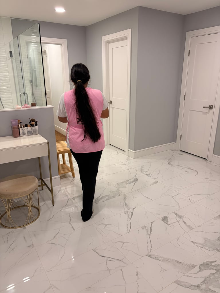 Woman with long dark hair wearing pink shirt standing in modern bathroom with marble flooring and white vanity
