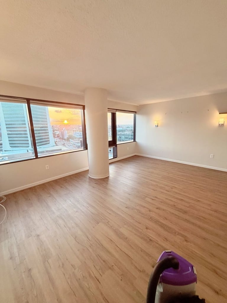 Empty high-rise apartment living room with wood flooring, large windows overlooking cityscape, white walls, and a central column