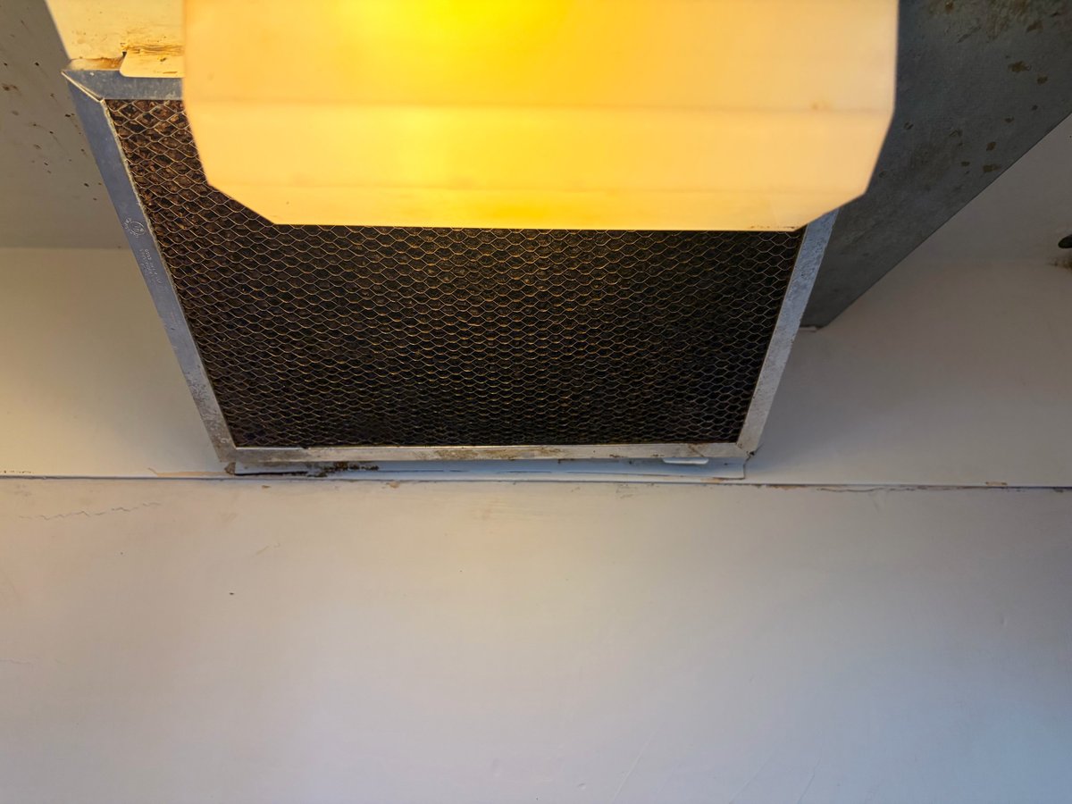 Recessed ceiling light fixture with warm yellow glow and black mesh diffuser panel installed in white drywall ceiling