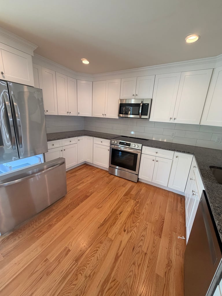 Modern kitchen with white cabinets, gray countertops, stainless steel appliances, and wood flooring