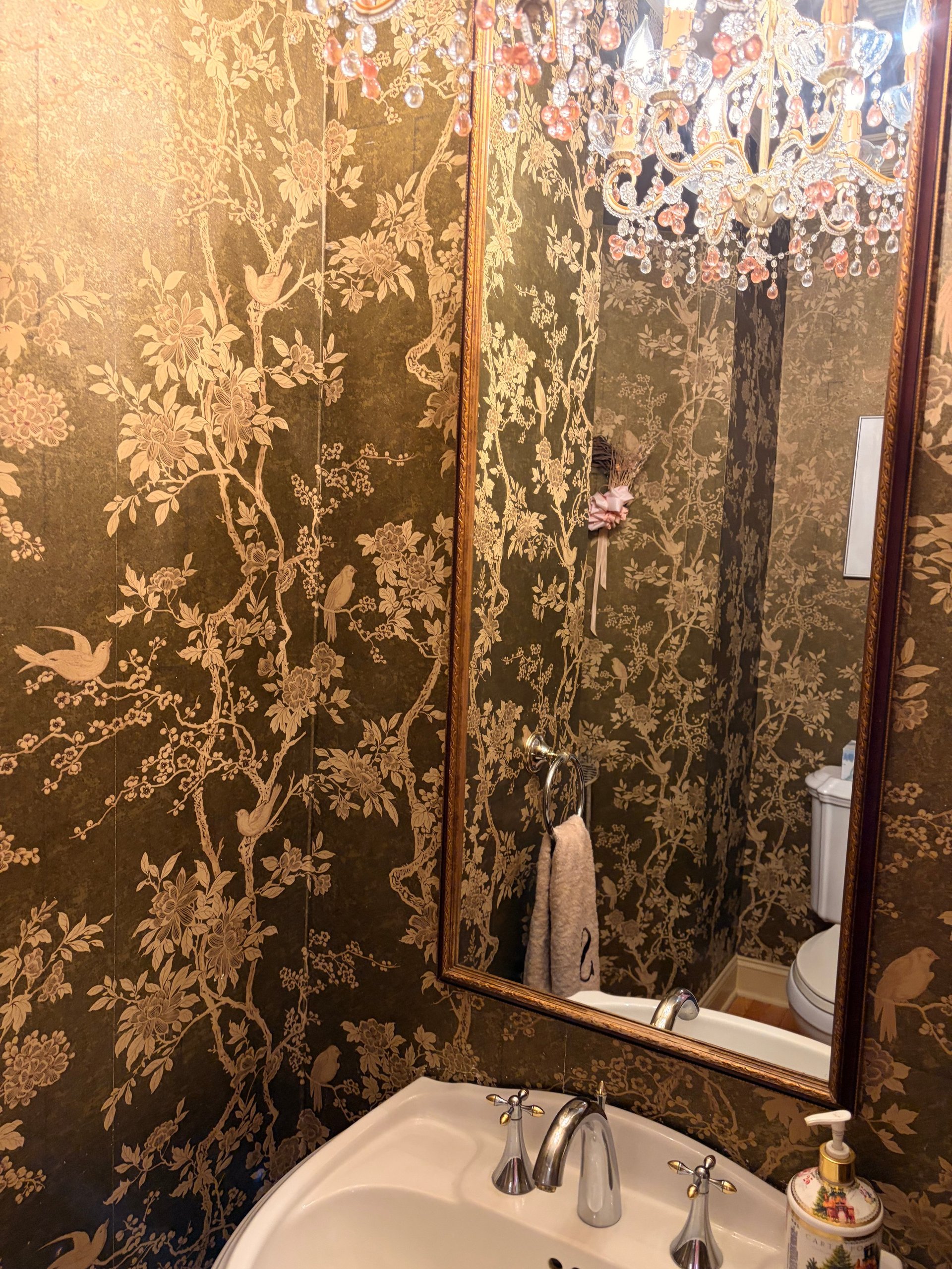 Bathroom sink with ornate dark wallpaper featuring botanical designs and gold accents, framed mirror, and towel rack
