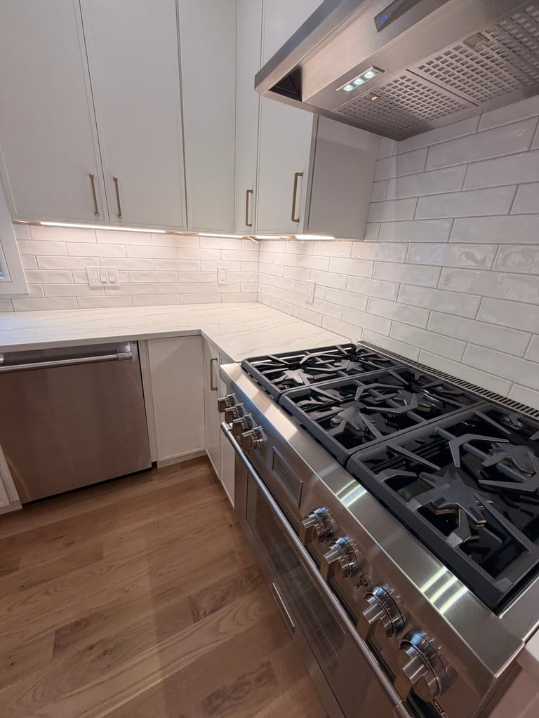 Modern kitchen with white subway tile backsplash, stainless steel gas range, white cabinetry, and wood flooring